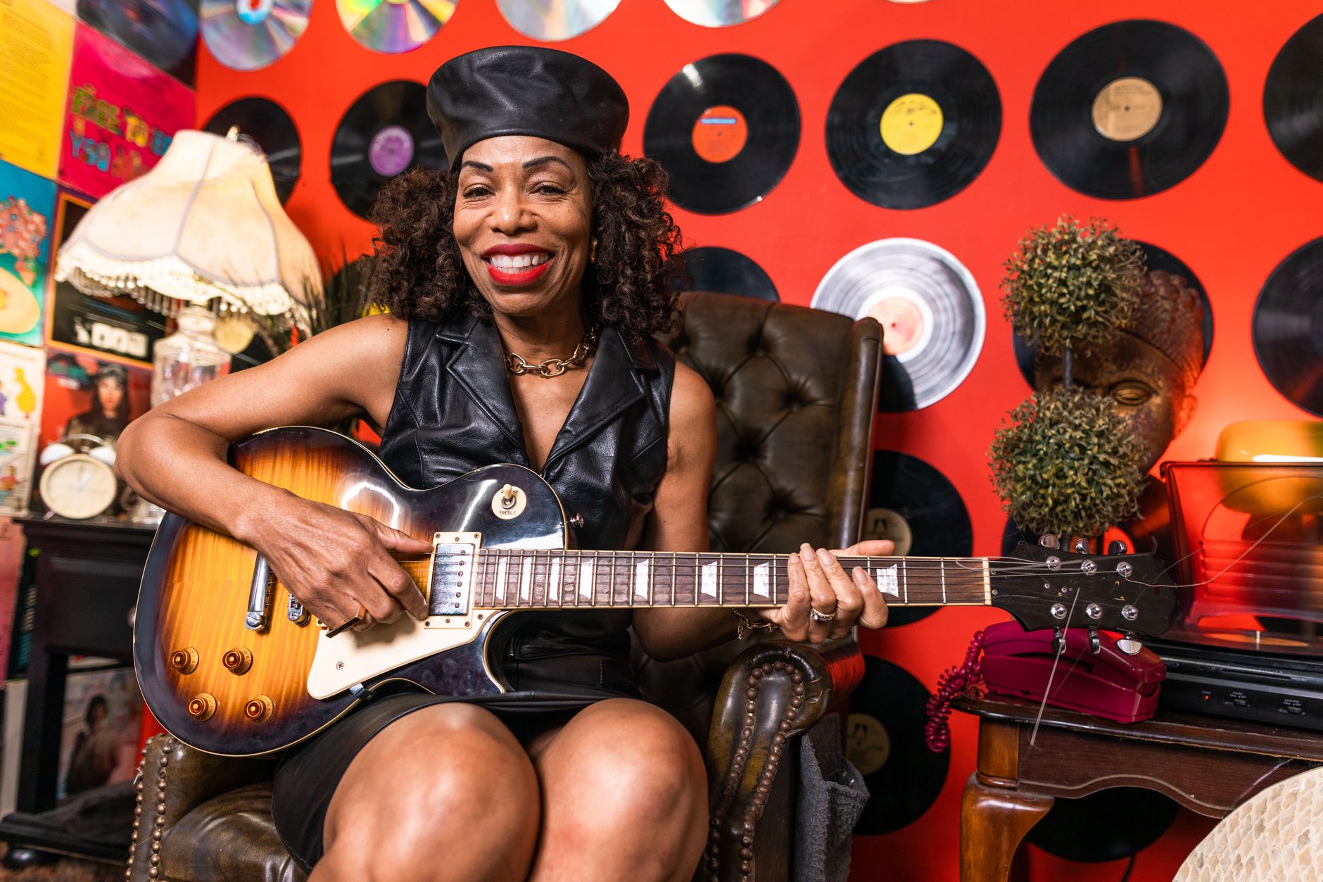 Smiling senior woman enjoying music, playing guitar in a retro-themed room.