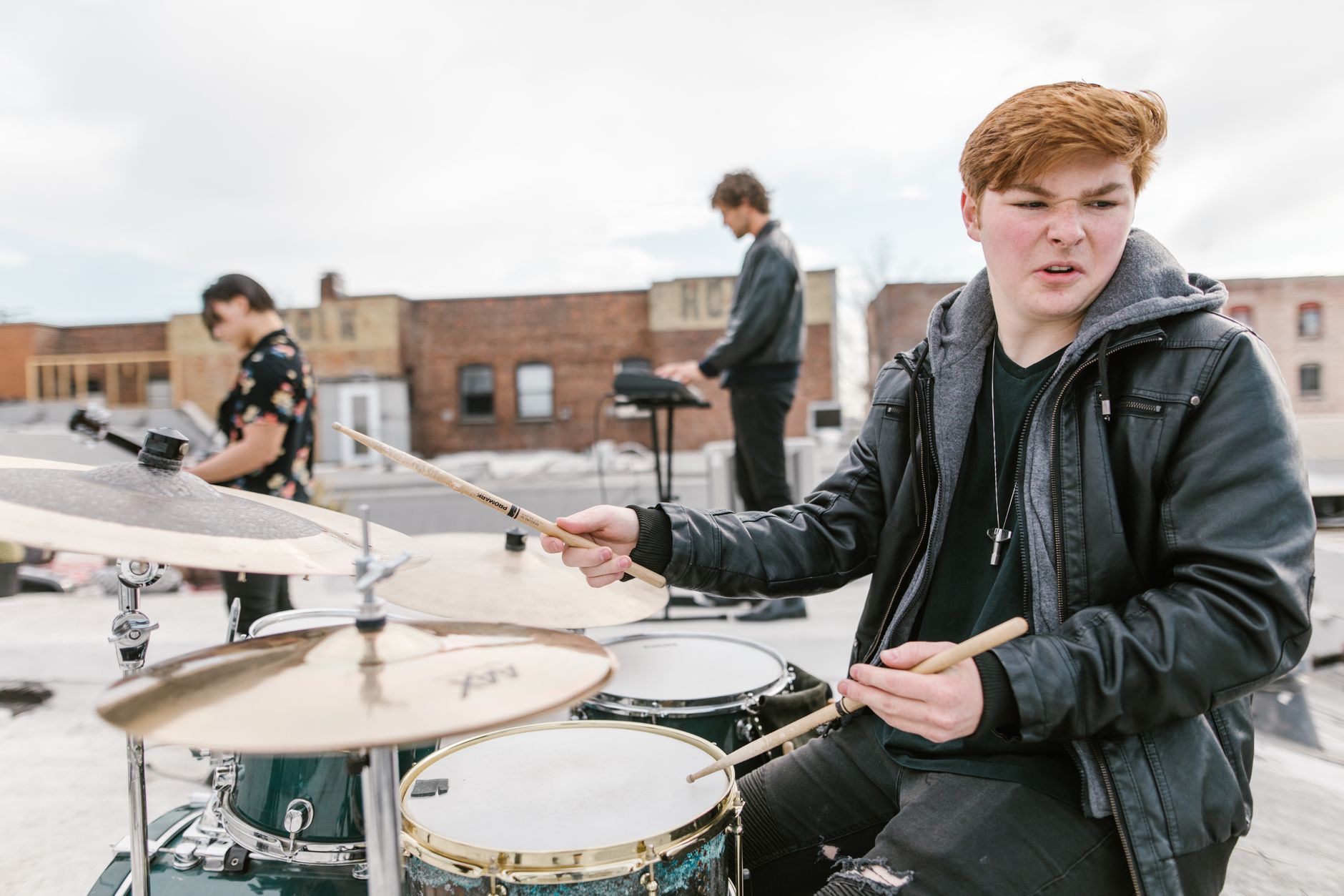 A young drummer energetically performs with a band on a rooftop, showcasing musical passion.