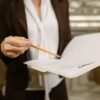 A businesswoman holds a contract, pointing with a pencil. Legal and corporate setting.