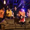 A diverse group of young adults enjoying video games together in a modern indoor setting with vibrant lighting.