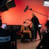 A behind-the-scenes look at a filming crew setting up a scene indoors with lighting equipment.