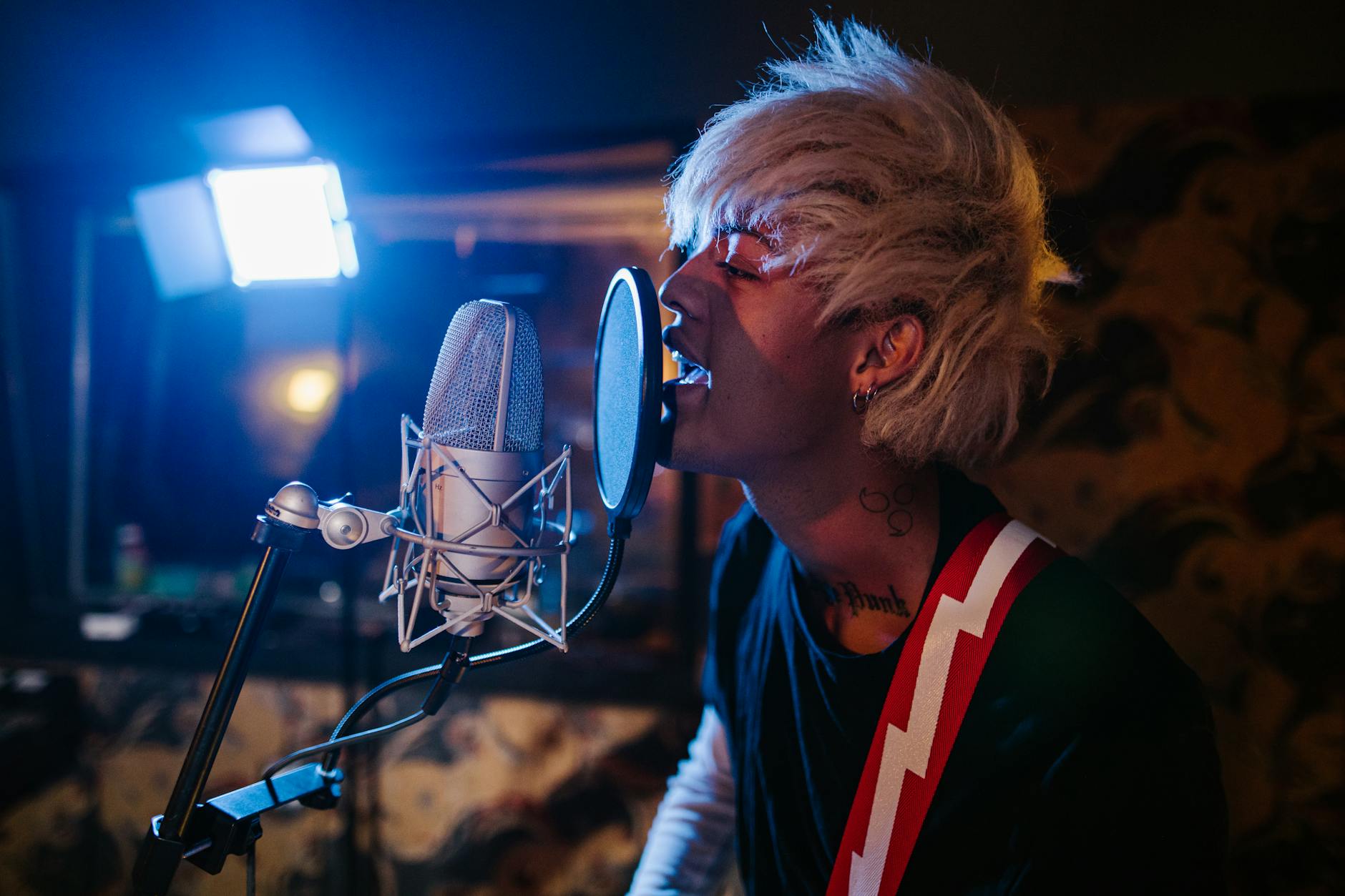 Young man passionately singing into a microphone in a moody recording studio setting.