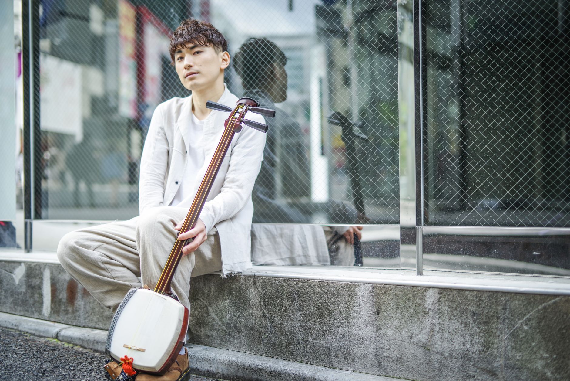 A young man sitting on a street, playing a shamisen, reflecting modern urban culture.