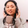 Female artist recording music in studio with condenser microphone and headphones.