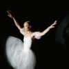 Graceful ballerina performing in white dress under dramatic lighting.