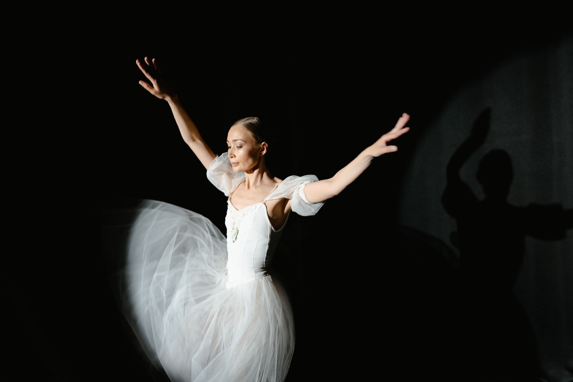 Graceful ballerina performing in white dress under dramatic lighting.