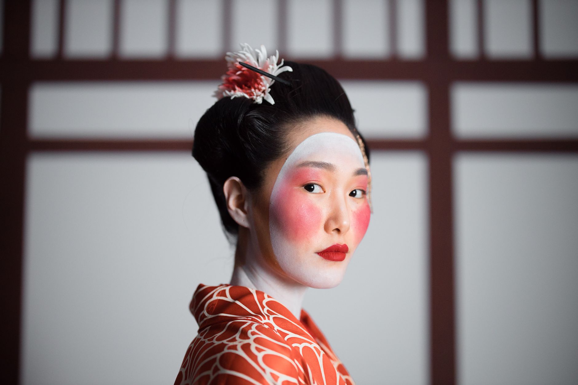 Portrait of a traditional geisha in elegant red kimono with striking makeup.
