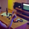 A tattooed man examines a photo in a dimly lit room with a retro TV.
