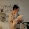 A mother multitasking with her newborn and phone indoors, surrounded by job ads on the wall.