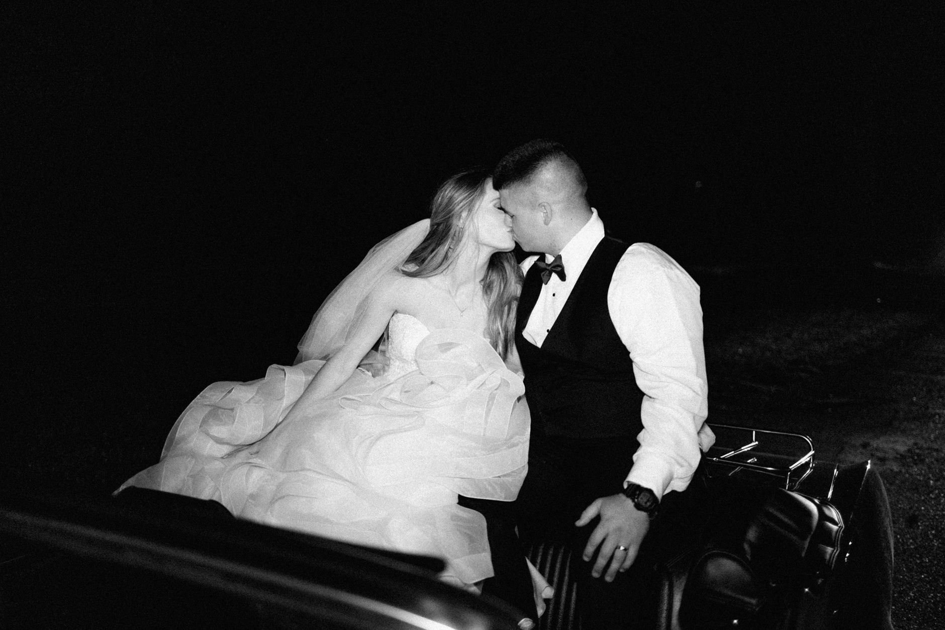 Romantic newlyweds kissing under the night sky in a classic car.