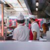 Chefs in uniforms working in an open restaurant kitchen, preparing food orders.