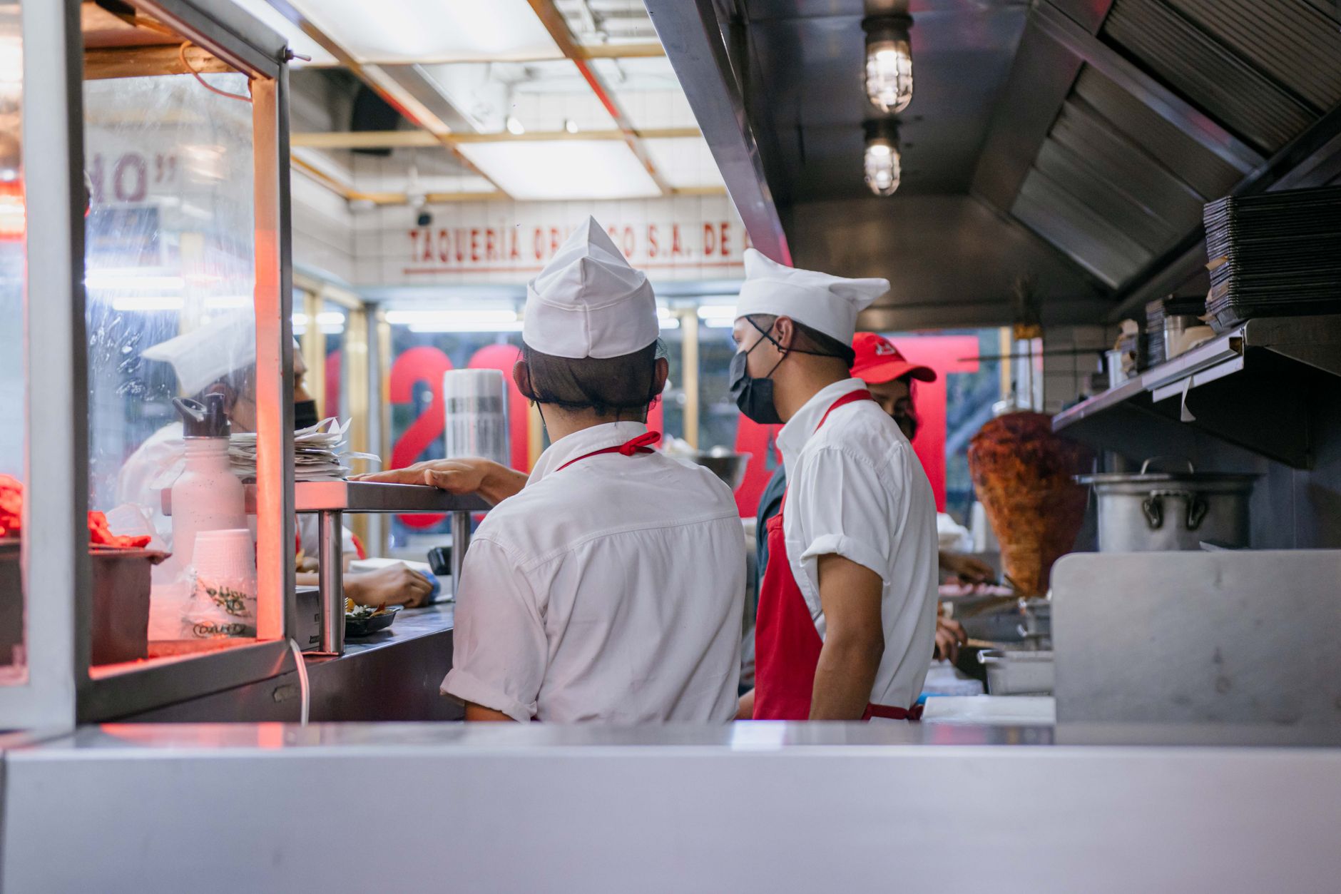 Chefs in uniforms working in an open restaurant kitchen, preparing food orders.