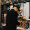 A senior man in a hat browsing magazines at a kiosk. Indoor setting with diverse print media.