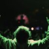 A person raises their hands conducting at a vibrant night concert.
