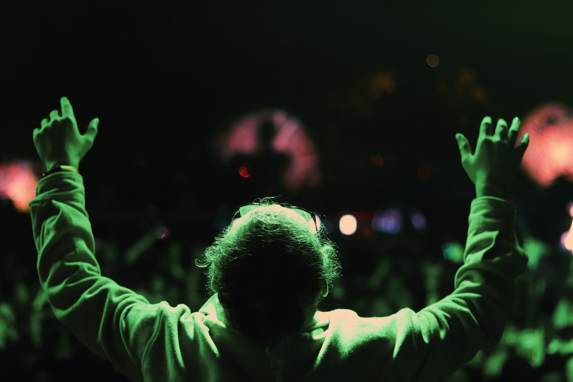 A person raises their hands conducting at a vibrant night concert.