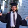 A surprised graduate poses outdoors in cap and gown, celebrating academic achievement.