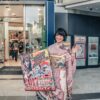 Asian woman in kimono holding promotional sign outside a store.