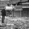 A man stands amidst ruins and debris following a natural disaster in an urban area.