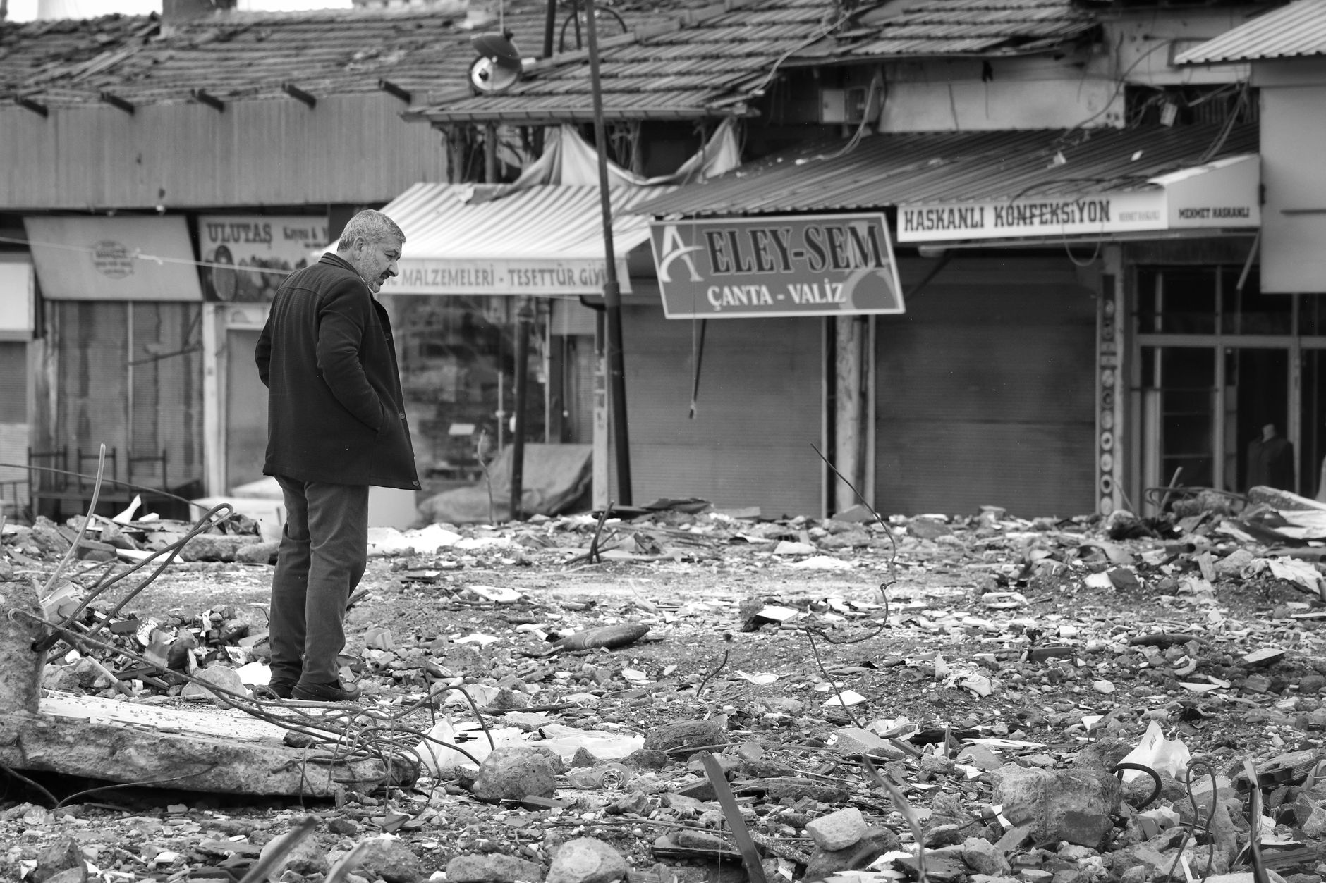 A man stands amidst ruins and debris following a natural disaster in an urban area.