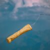 Yellow windsock blowing in the wind, mounted on a pole against a cloudy blue sky.