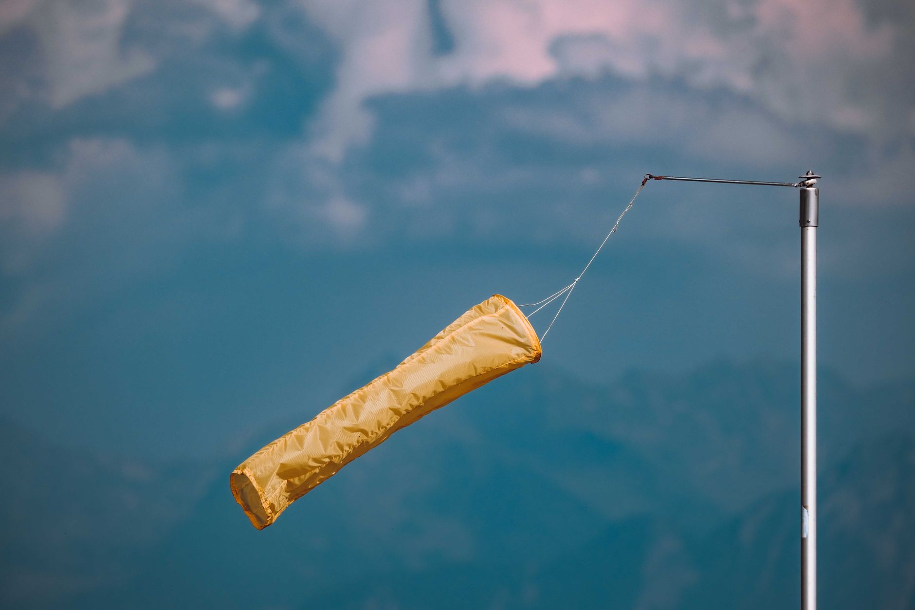 Yellow windsock blowing in the wind, mounted on a pole against a cloudy blue sky.