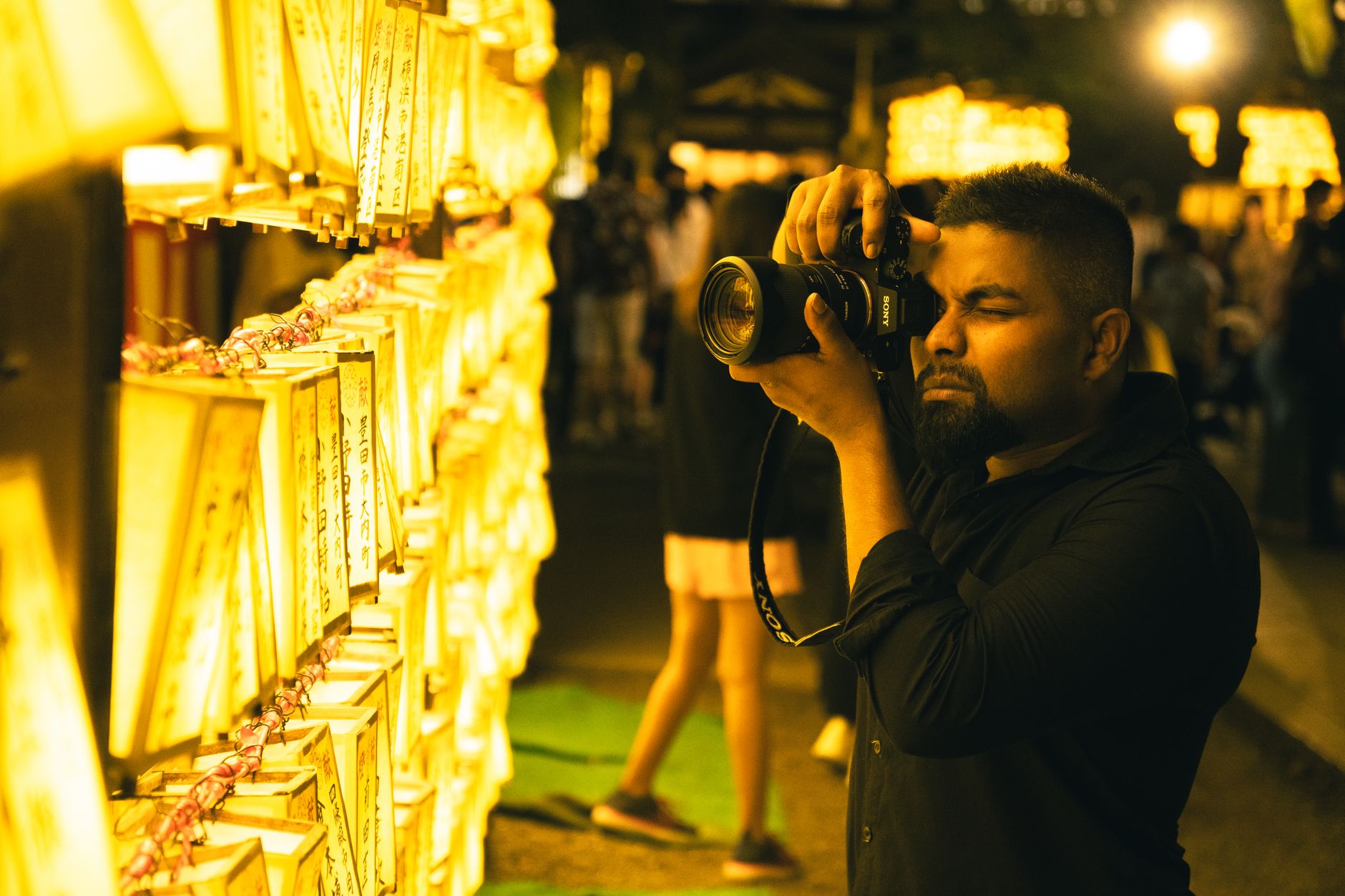 Man photographing glowing Mitama lanterns at a Japanese festival, showcasing cultural traditions and night ambiance.