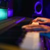 Hands playing a keyboard in a vibrant music studio with colorful lighting.