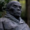 A close-up of a historic Japanese monk statue situated in a tranquil forest setting, capturing cultural essence.