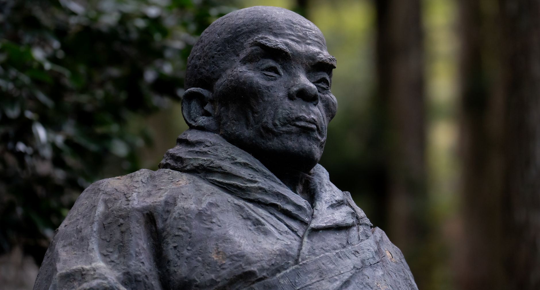 A close-up of a historic Japanese monk statue situated in a tranquil forest setting, capturing cultural essence.
