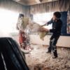 Two people enjoy a fun pillow fight indoors with feathers scattering everywhere.