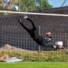 Dynamic action shot of a goalkeeper making a high save during a soccer game outdoors.