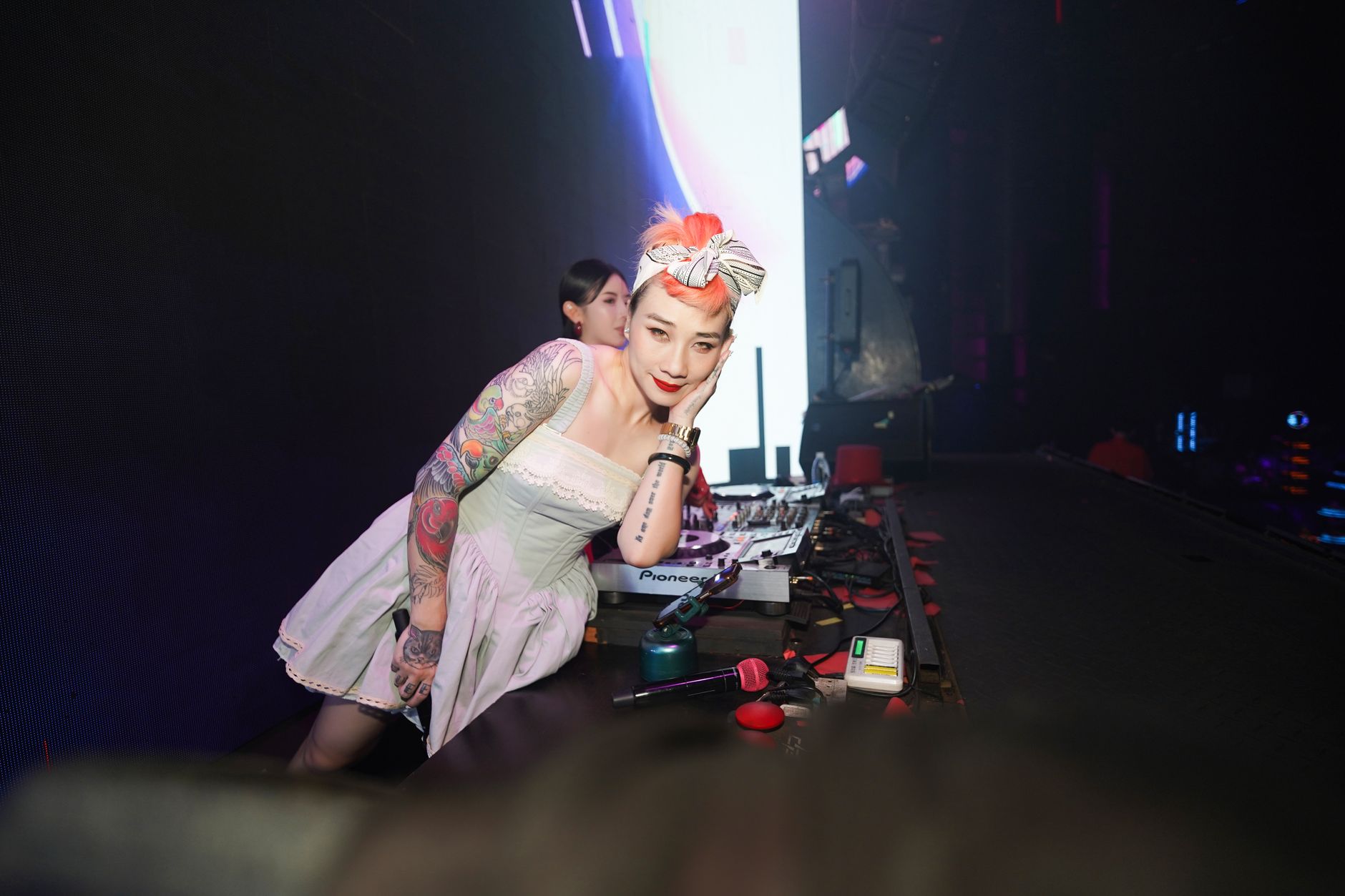 A female DJ with colorful tattoos and hair entertaining a lively nightclub audience.