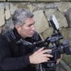 Experienced filmmaker adjusting a professional video camera outdoors.