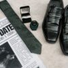 Flat lay of wedding essentials with shoes, tie, newspaper, and rings.