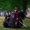 Three individuals in samurai cosplay pose with swords in a serene park, blending historical elegance and natural beauty.