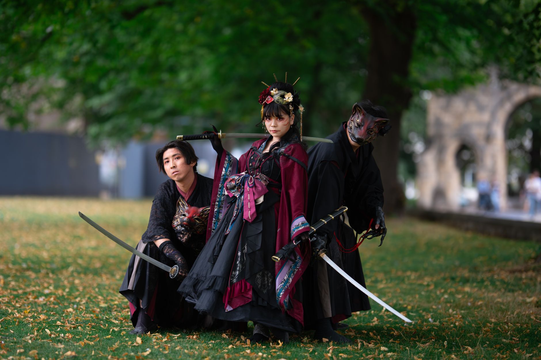 Three individuals in samurai cosplay pose with swords in a serene park, blending historical elegance and natural beauty.