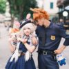 Cosplay couple dressed as animal characters from a popular Disney movie, posing outdoors with plush toys.