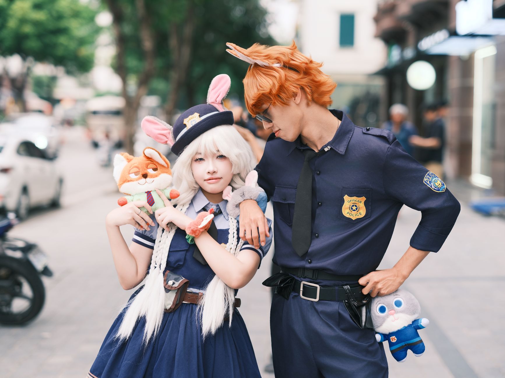 Cosplay couple dressed as animal characters from a popular Disney movie, posing outdoors with plush toys.