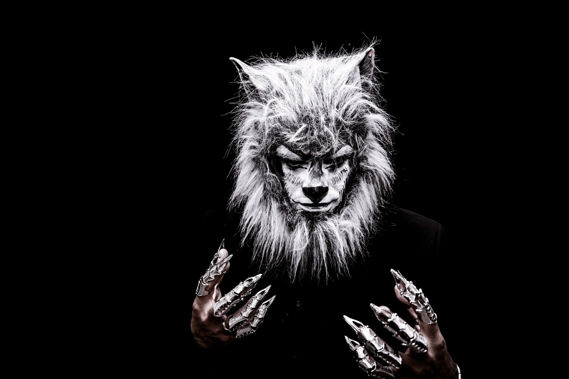 Striking portrait of an adult in a realistic werewolf costume with metallic claws against a black background.
