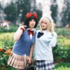 Two women in colorful cosplay outfits posing playfully outdoors in a garden setting.