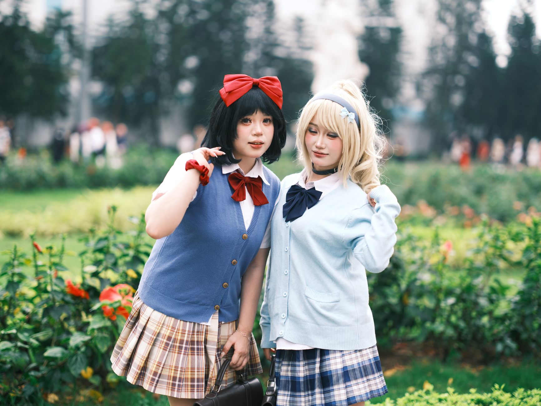 Two women in colorful cosplay outfits posing playfully outdoors in a garden setting.