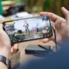 Person playing PUBG on smartphone outdoors with charging cable attached.