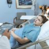 Caucasian woman in hospital bed receiving care from healthcare professional.