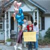 Family joyfully announcing pregnancy with balloons in front of house.