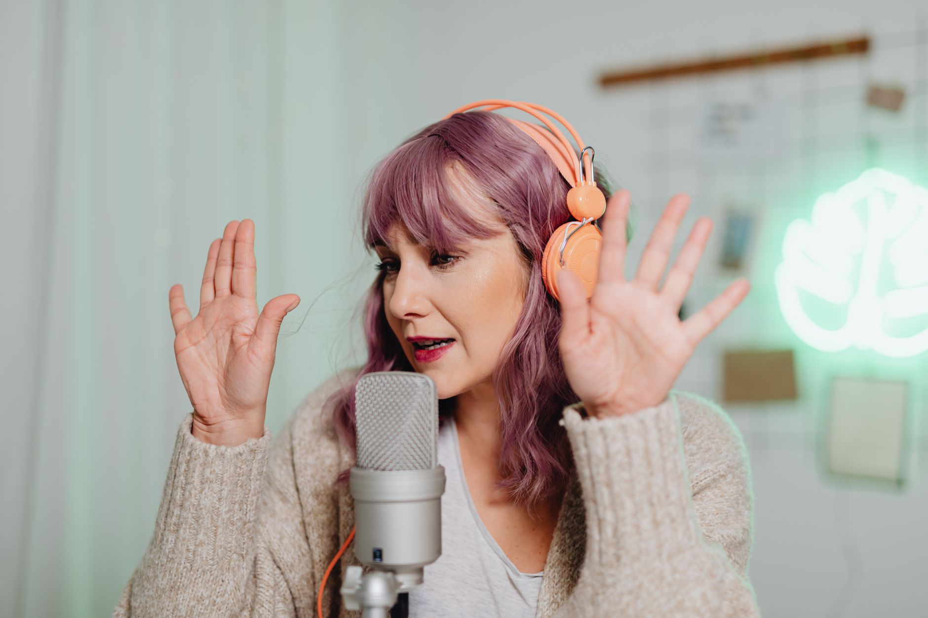 A woman podcasting in a studio setting with a microphone and headphones, gesturing expressively.