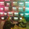 A cyberpunk inspired setting featuring two people with retro TVs displaying colorful test screens.
