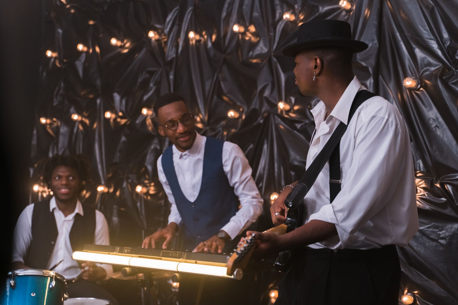 Three musicians perform with piano, guitar, and drums in a stylish decorated room.
