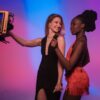 Two women dancing joyously with colorful studio background lighting.