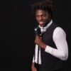 Smiling singer holding a vintage microphone against a black background.