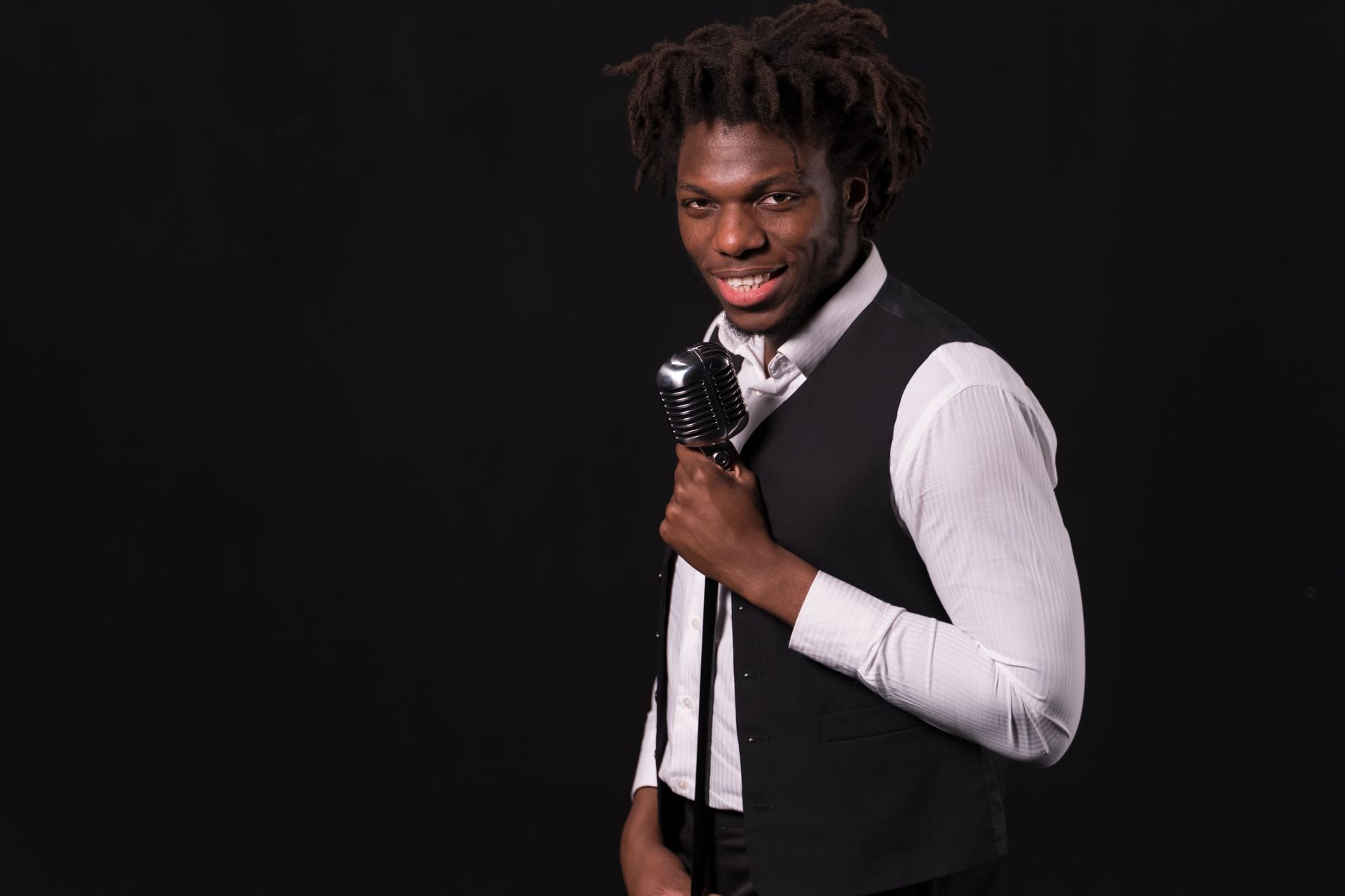 Smiling singer holding a vintage microphone against a black background.
